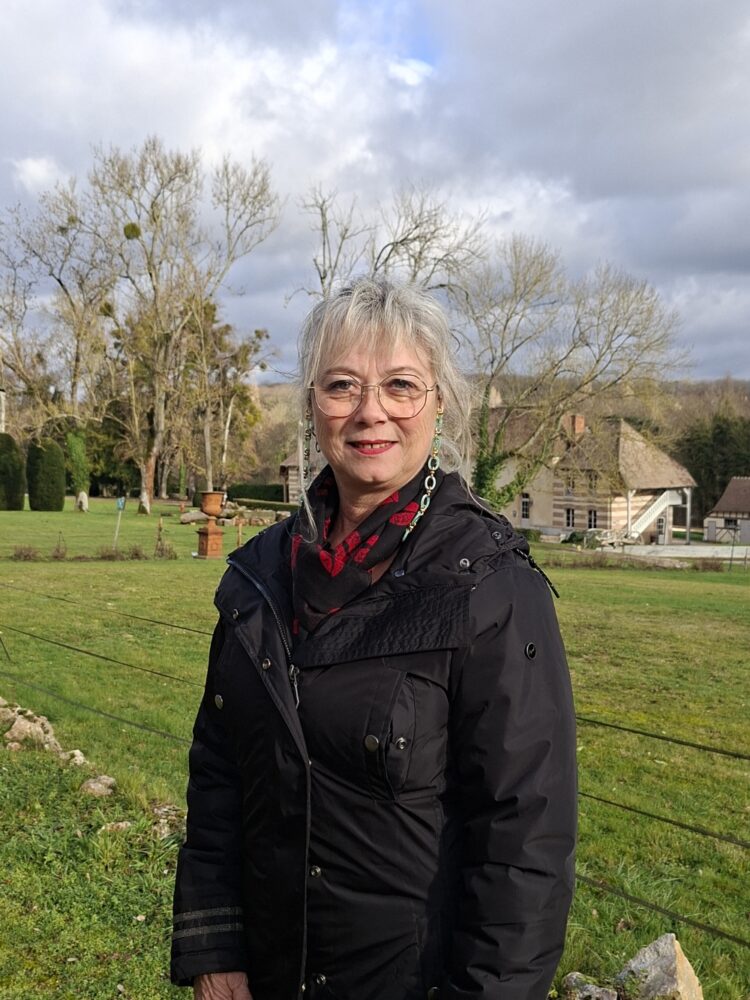 Madame CARETTE, en fond le décor d'un beau paysage saint-aubinois, un jour de ciel clairsemé